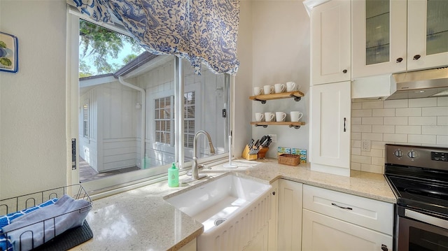 kitchen featuring stainless steel range with electric cooktop, a sink, tasteful backsplash, under cabinet range hood, and glass insert cabinets