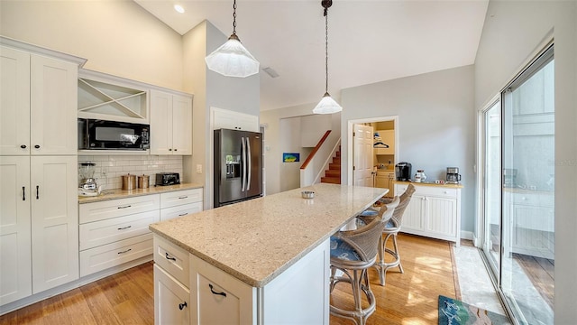 kitchen featuring stainless steel refrigerator with ice dispenser, black microwave, a center island, light wood-type flooring, and decorative backsplash