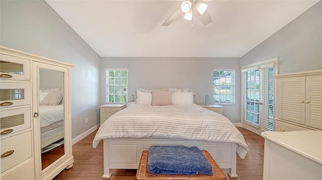 bedroom with vaulted ceiling, wood finished floors, multiple windows, and access to outside