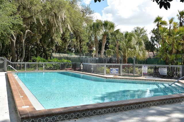 community pool with fence and view of wooded area