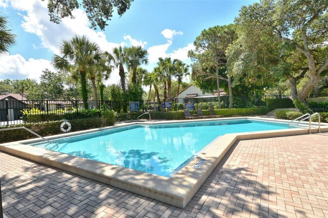 community pool featuring fence, a patio, and view of scattered trees