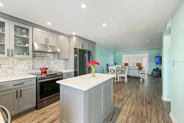 kitchen featuring stainless steel appliances, under cabinet range hood, gray cabinets, decorative backsplash, and wood finished floors