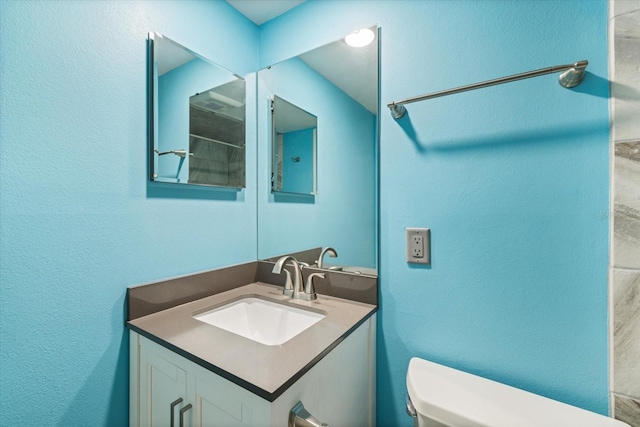 bathroom featuring toilet, vanity, and a textured wall