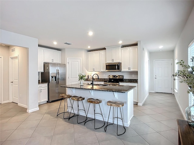 kitchen featuring stainless steel appliances, a sink, light tile patterned floors, a breakfast bar, and dark stone countertops