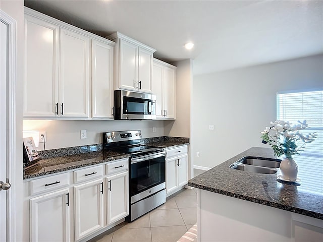 kitchen with appliances with stainless steel finishes, white cabinets, dark stone counters, light tile patterned floors, and recessed lighting