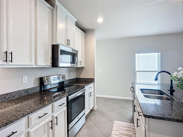kitchen featuring stainless steel appliances, a sink, white cabinets, light tile patterned floors, and dark stone countertops