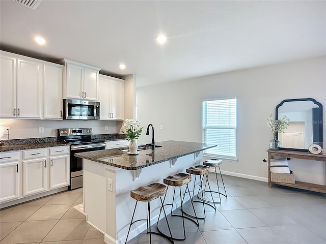 kitchen featuring appliances with stainless steel finishes, a sink, light tile patterned floors, dark stone countertops, and recessed lighting