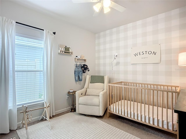 bedroom featuring baseboards, wallpapered walls, a nursery area, a ceiling fan, and carpet floors