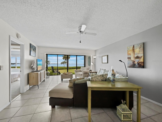 living area featuring light tile patterned floors, a ceiling fan, a textured ceiling, and baseboards