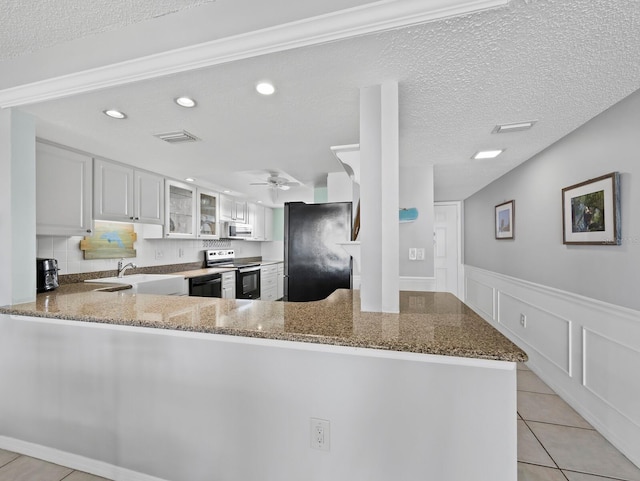 kitchen with black appliances, stone countertops, a peninsula, ceiling fan, and a wainscoted wall