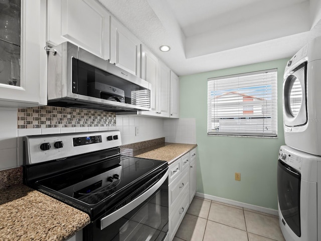 kitchen featuring stainless steel appliances, stacked washer and clothes dryer, backsplash, white cabinetry, and baseboards