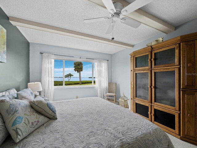 bedroom with beam ceiling, a textured ceiling, carpet, and ceiling fan