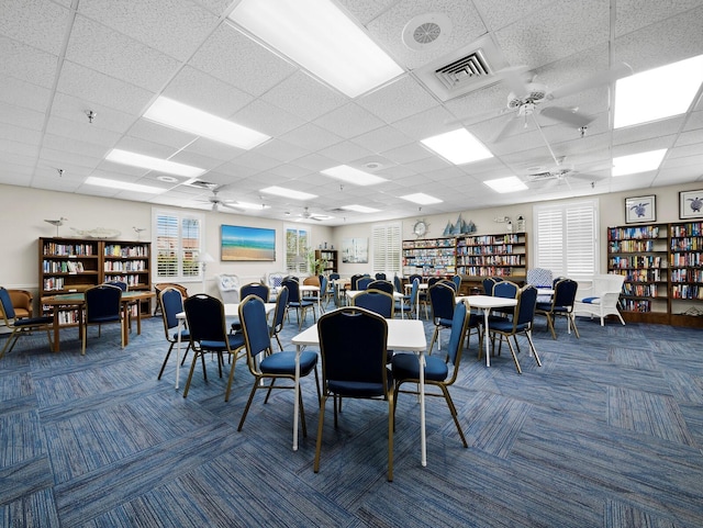 carpeted dining area featuring ceiling fan and a drop ceiling