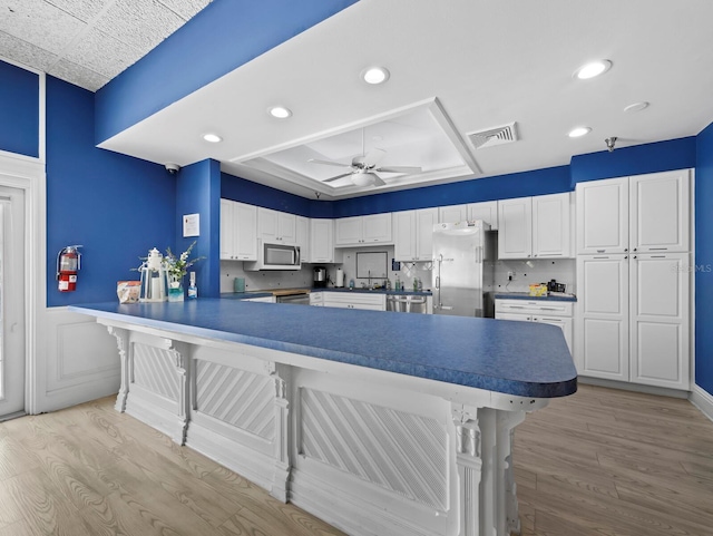 kitchen featuring appliances with stainless steel finishes, light wood-style floors, ceiling fan, a kitchen bar, and a wainscoted wall