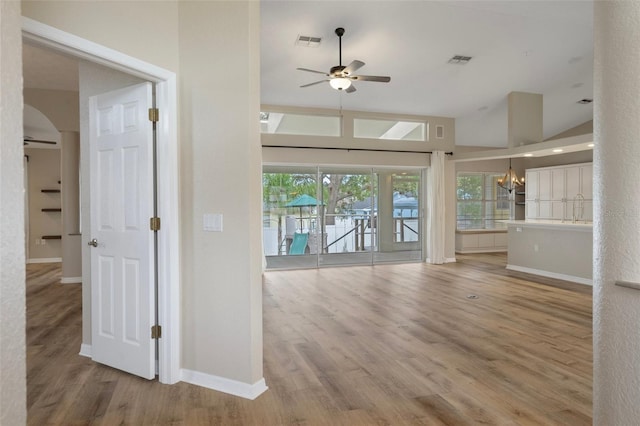 unfurnished living room featuring ceiling fan, a chandelier, wood finished floors, and baseboards