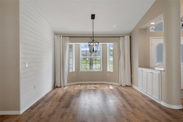 unfurnished dining area with a chandelier, wood finished floors, and baseboards