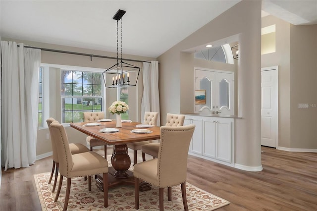 dining space with a chandelier, light wood-type flooring, vaulted ceiling, and baseboards