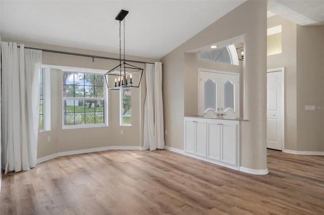 unfurnished dining area with lofted ceiling, a chandelier, light wood finished floors, and baseboards