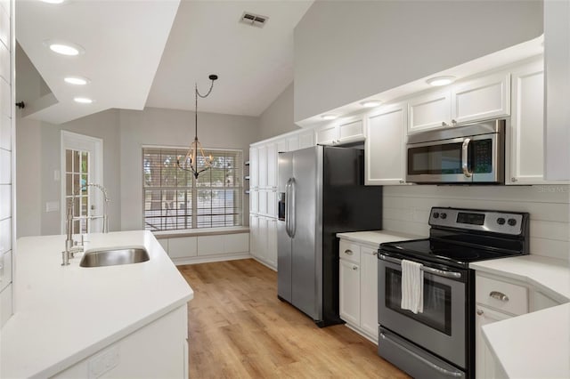kitchen with appliances with stainless steel finishes, a sink, lofted ceiling, white cabinetry, and light wood-style flooring