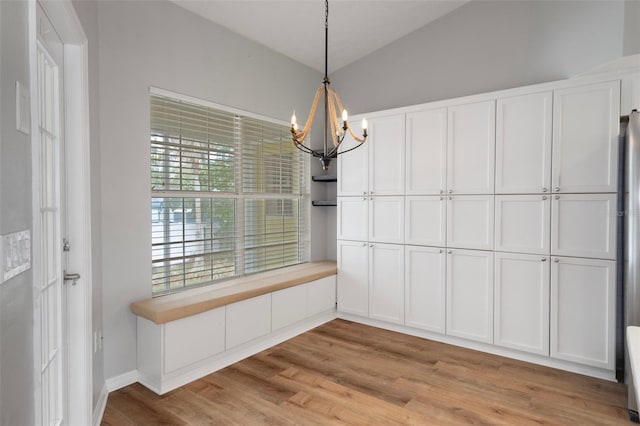 unfurnished dining area featuring a chandelier, light wood-style floors, and lofted ceiling