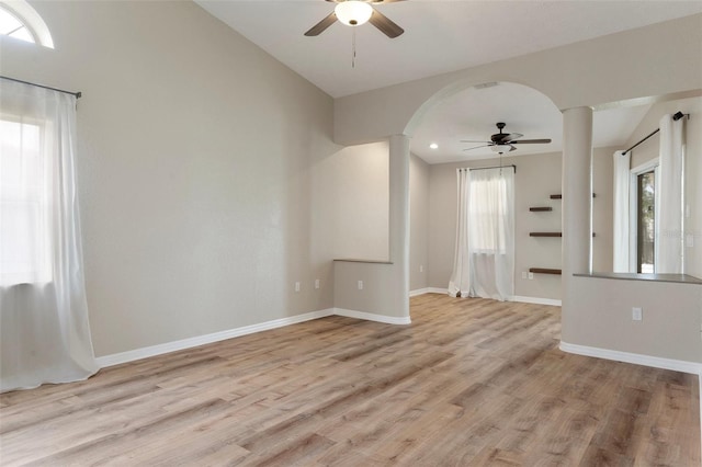 empty room featuring a ceiling fan, ornate columns, light wood-style floors, baseboards, and arched walkways