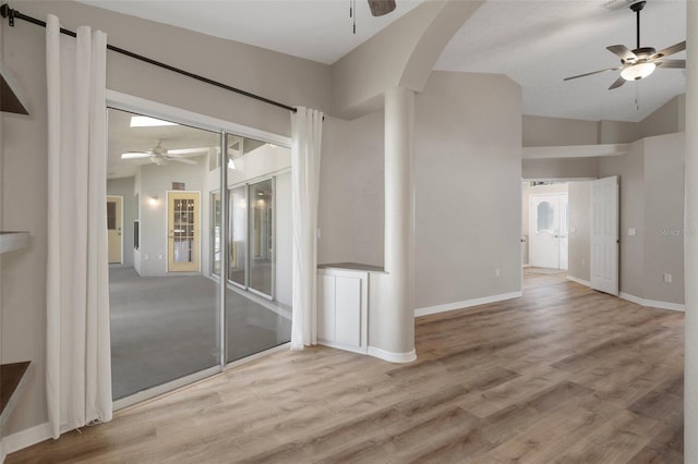 empty room featuring a ceiling fan, vaulted ceiling, wood finished floors, arched walkways, and baseboards
