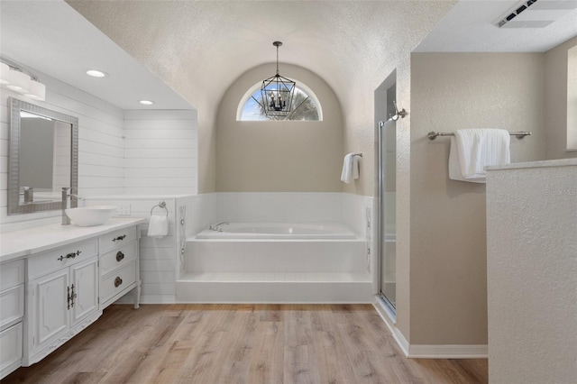bathroom featuring a textured wall, a bath, wood finished floors, vanity, and a chandelier