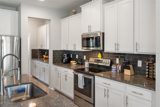 kitchen with appliances with stainless steel finishes, a sink, white cabinetry, decorative backsplash, and dark stone counters