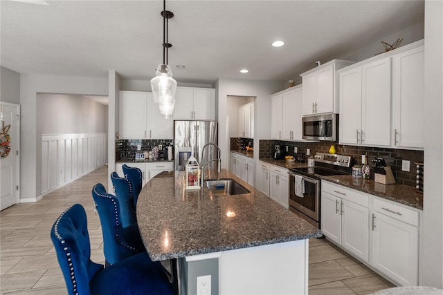 kitchen featuring appliances with stainless steel finishes, a sink, decorative backsplash, a kitchen island with sink, and white cabinets