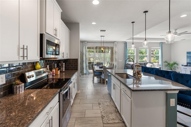 kitchen featuring appliances with stainless steel finishes, a sink, open floor plan, decorative backsplash, and recessed lighting