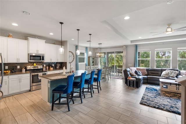 kitchen featuring appliances with stainless steel finishes, open floor plan, decorative backsplash, a ceiling fan, and a kitchen breakfast bar