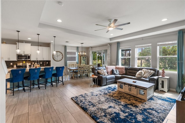 living area featuring a ceiling fan, a tray ceiling, recessed lighting, and a chandelier