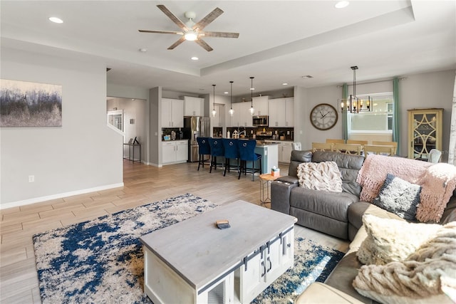 living room with a chandelier, a ceiling fan, light wood finished floors, baseboards, and recessed lighting