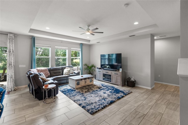 living area featuring a tray ceiling, a ceiling fan, healthy amount of natural light, baseboards, and recessed lighting
