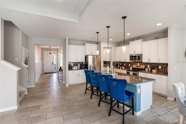 kitchen featuring appliances with stainless steel finishes, a sink, tasteful backsplash, a kitchen bar, and white cabinetry