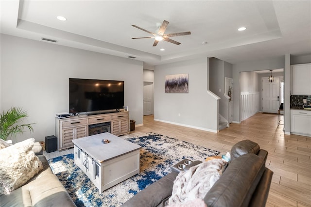 living area featuring a raised ceiling, a ceiling fan, recessed lighting, light wood-style floors, and stairs