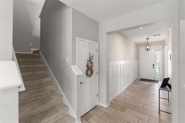 foyer featuring stairs, a chandelier, wood tiled floors, a wainscoted wall, and baseboards