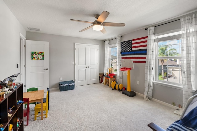 game room with plenty of natural light, a ceiling fan, carpet, and a textured ceiling