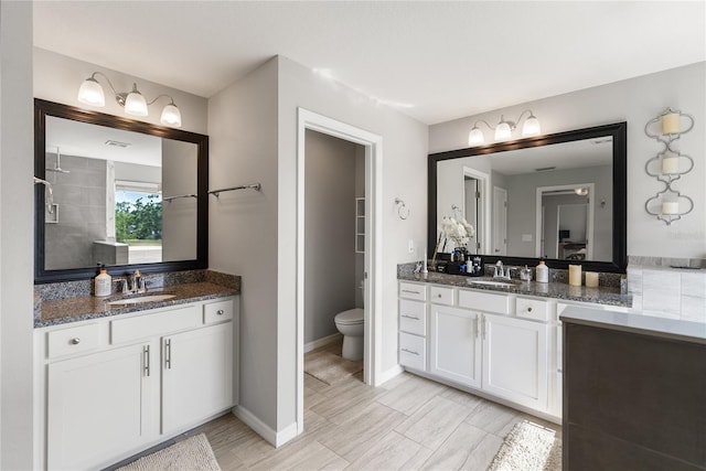 full bath featuring two vanities, toilet, and baseboards