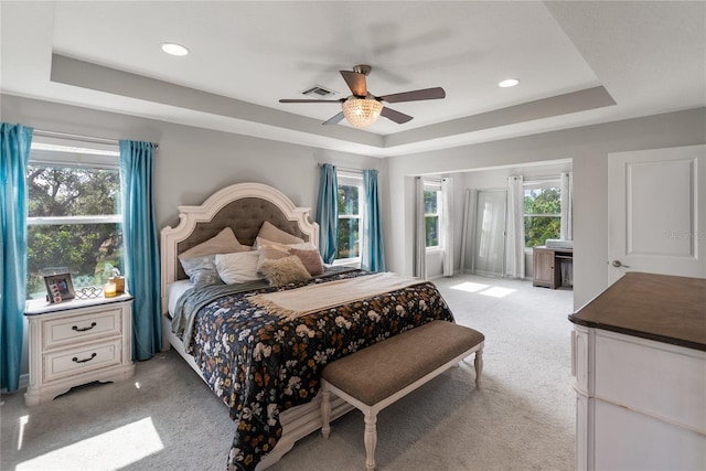 bedroom with a raised ceiling, light colored carpet, multiple windows, and recessed lighting
