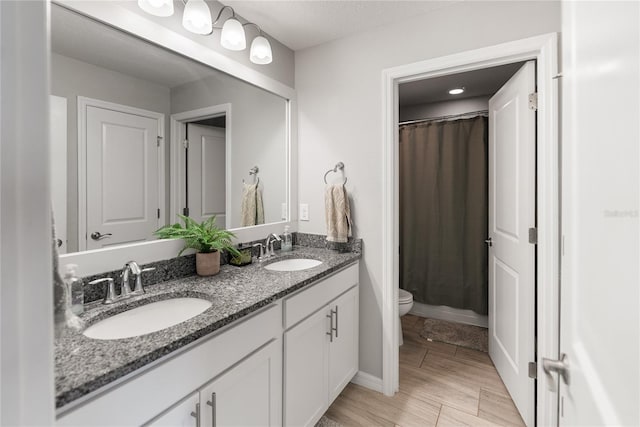 bathroom with toilet, double vanity, a shower with curtain, and wood finished floors