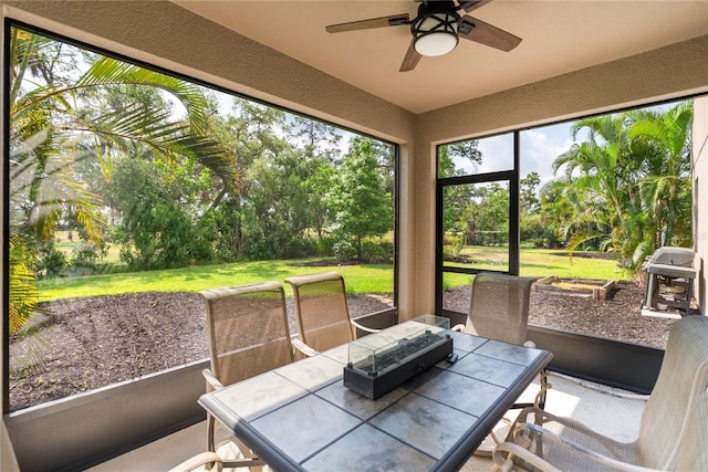 sunroom / solarium with a ceiling fan, outdoor dining space, and view of scattered trees