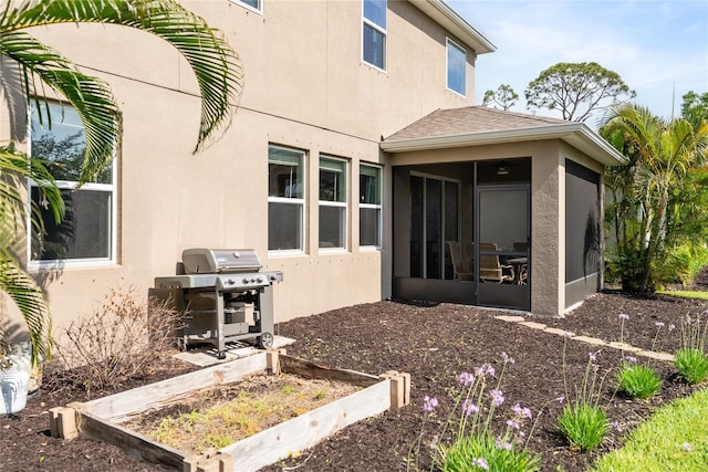 back of house with a sunroom, stucco siding, a garden, and roof with shingles