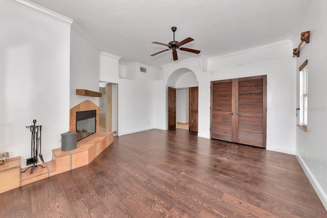 unfurnished living room with ceiling fan, a tile fireplace, arched walkways, wood finished floors, and crown molding