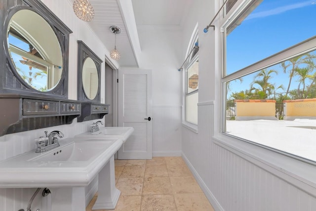 bathroom with stone tile flooring, baseboards, wainscoting, and a sink