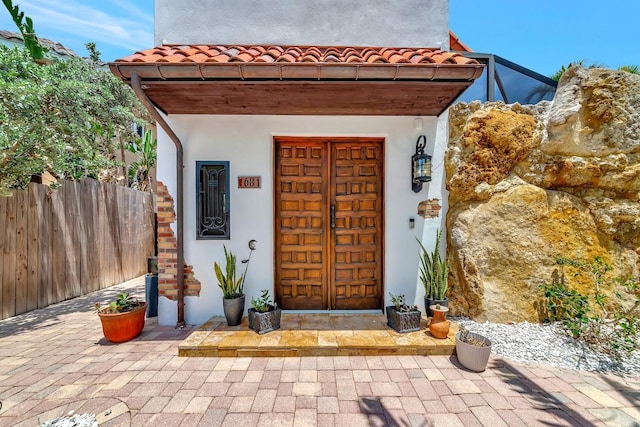 property entrance with stucco siding, fence, and a tile roof