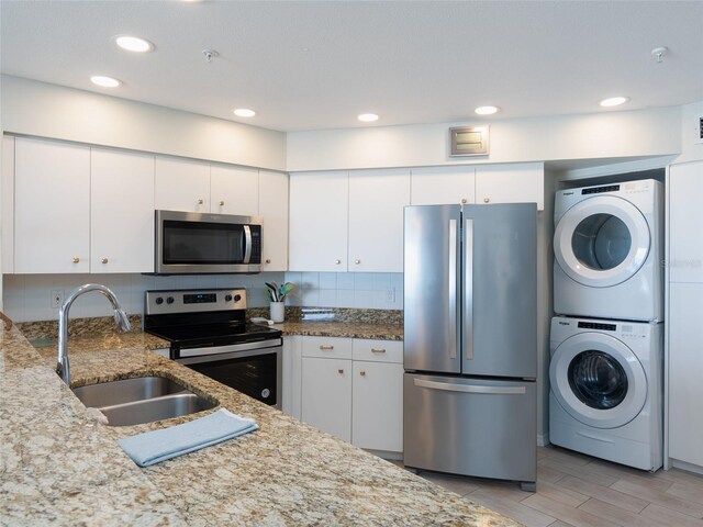 2400 N Beach Rd Unit 1, Englewood, FL 34223 - kitchen featuring stainless steel appliances, stacked washer and clothes dryer, a sink, white cabinets, and backsplash