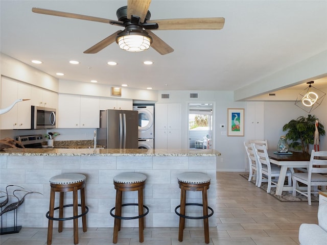 2400 N Beach Rd Unit 1, Englewood, FL 34223 - kitchen with estacked washer and dryer, appliances with stainless steel finishes, a peninsula, light stone counters, and a kitchen breakfast bar
