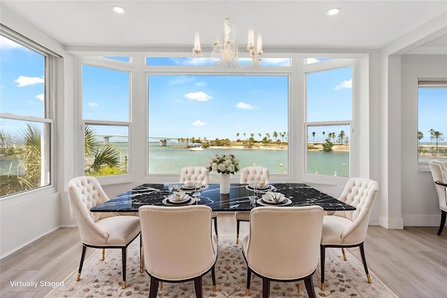 dining space featuring a water view, wood finished floors, baseboards, recessed lighting, and a chandelier