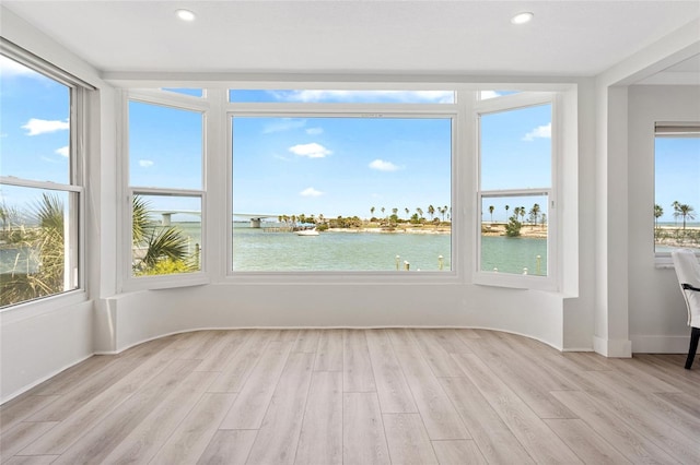 unfurnished sunroom featuring a water view, wood finished floors, recessed lighting, and baseboards